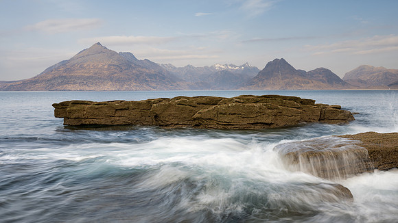 Waves breaking on the rocky shoreline of Elgol on the Isle of Skye with mountains in the background