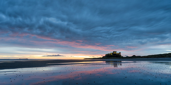 Bamburgh Castle and the beach with dramatuic clouds and sunrise with great orange glow in the sky