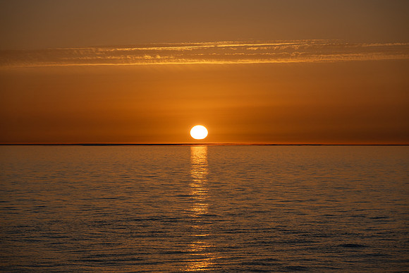Golden sun sets on a calm sea on a warm summers evening
