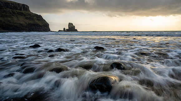 Huge smooth black lava pebbles shimmer through the waves. at Talisker Bay on the Isle of Skye