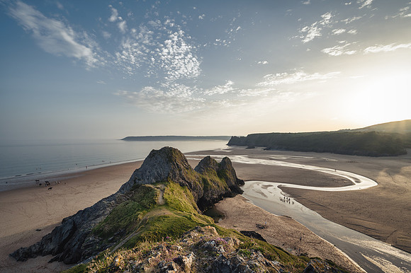 The three cliffs illuminated by the setting sun on Threee Cliffs Bay om the Gower Peninsula with a group of ponies talking an evening run on the beach below.
