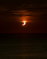 Observers slowly begin to depart in the boats as the setting sun emerges from behind the moon.