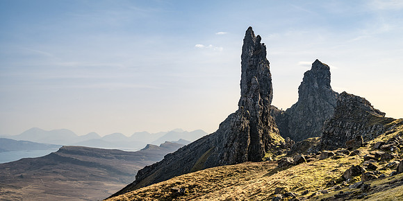 A man appears very small standing at the base of the Old Man of Storr pinnacles on Isle of Skye.