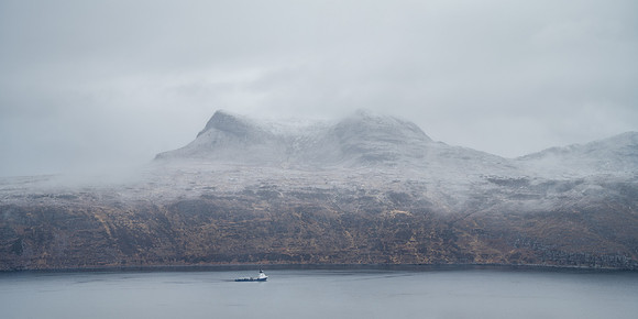 A boat sits on the loch with overnight snow covering Beinn Ghobhlach in the misty Scottish Highlands