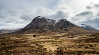 Small white cottage stands at the base of Buachaille Etive Mòr in the Scottish Highlands in Scotland.
