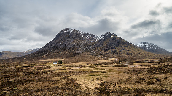 Small white cottage stands at the base of Buachaille Etive Mòr in the Scottish Highlands in Scotland.