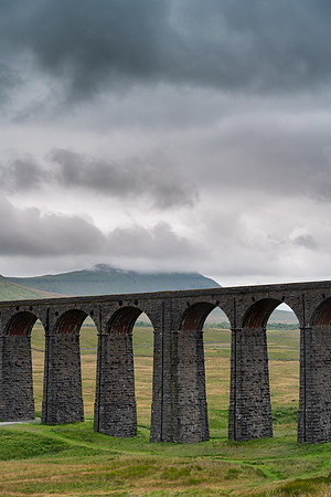 Arches of the Ribblehead Viaduct stretch away across the valley on a dark stormy day.