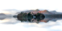Derwent Isle is reflected in a calm misty Derwentwater infront of Catbells during a spring sunrise