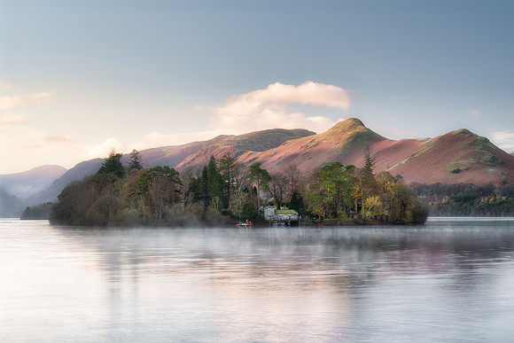 Derwent Isle is reflected in a calm misty Derwentwater infront of Catbells at sunrise during Autumn.