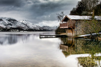 Pooley Bridge boat house reflected in Ullswater with snow capped mountains in the background.