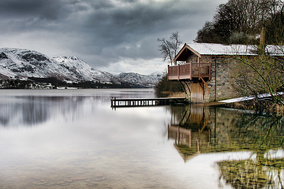 Pooley Bridge boat house reflected in Ullswater with snow capped mountains in the background.