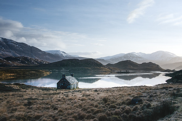 A boat house sits on the shore of loch Stack overlooking snow covered mountains of the Scottish Highlands.