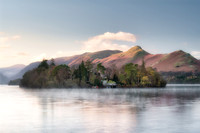 Derwent Isle is reflected in a calm misty Derwentwater infront of Catbells at sunrise during Autumn..