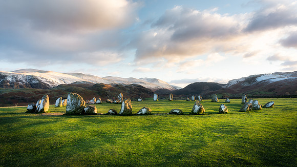 Sunset at Castlerigg Stone Circle with snow covered mountains and long shadows.