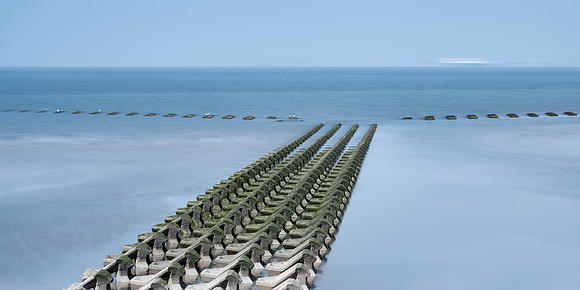 long exposure image of sea defences with birds sitting on them and a boat moving on the sea horizon at New Brighton.