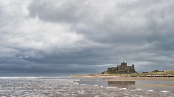 Bamburgh Castle reflected in the sand as the tide goes out at Bamburgh beach on a stormy day in Northumberland.