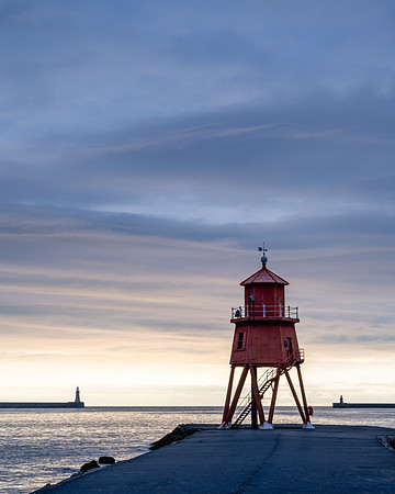 Sunrise at Tynemouth with Herd Groyne Lighthouse and Tynemouth lighthouse against an orange sky.