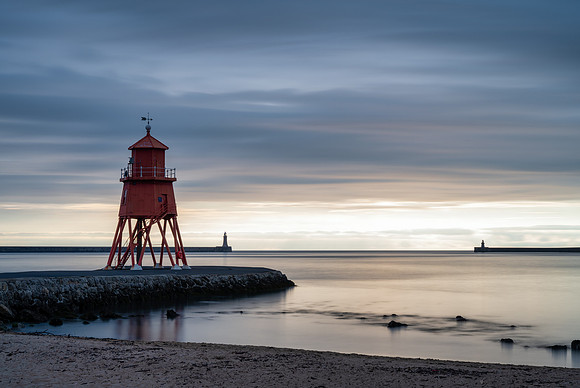 Sunrise at Tynemouth with Herd Groyne Lighthouse and Tynemouth lighthouse against an orange sky.