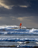 Wind surfer battles fierce waves against dark skies at the end of a storm in Cornwall.