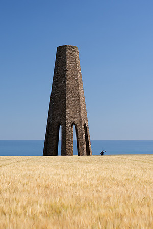 A man standing in a field of wheat takes a selfie at the base of Daymark Tower in Devon.