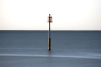 Long exposure image of a lone sea bird warming itself on top of a marker post at sunrise at Dawlish Warren in Devon.