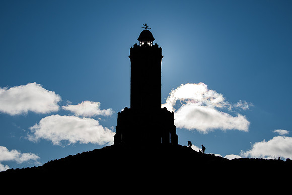 Silhouette of two walkers climbing up to Darwen Tower on a sunny day..