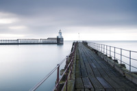 A derelict pier extends into the horizon over early morning calm seas at Blyth Lighthouse.
