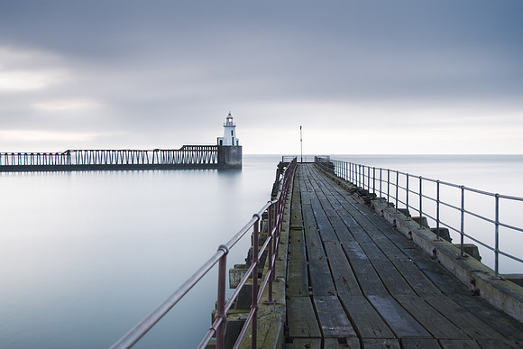 A derelict pier extends into the horizon over early morning calm seas at Blyth Lighthouse.