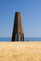 A man standing in a field of wheat takes a selfie at the base of Daymark Tower in Devon.