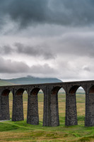 Arches of the Ribblehead Viaduct stretch away across the valley on a dark stormy day.