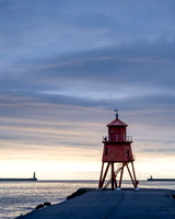 Sunrise at Tynemouth with Herd Groyne Lighthouse and Tynemouth lighthouse against an orange sky.