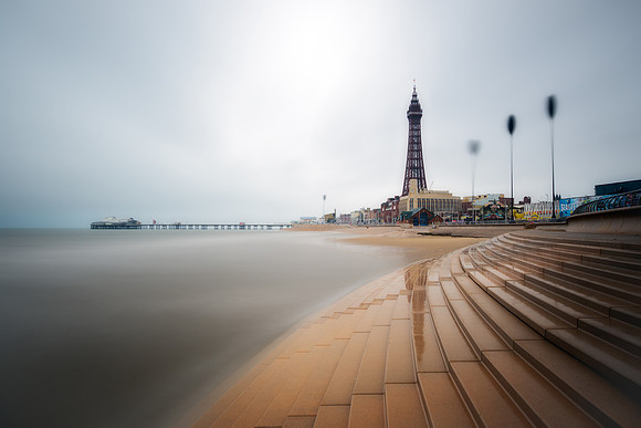 Long exposure image of steps down to the sea infront of Blackpool Tower and North Pier.