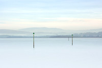 Three marker posts in the sea on a misty Morecambe bay.