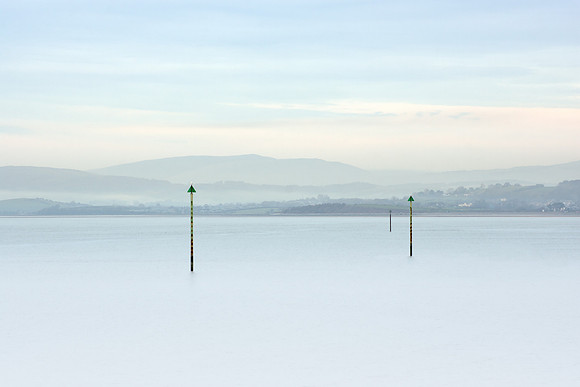 Three marker posts in the sea on a misty Morecambe bay.