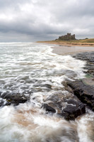 Waves crash against the rocks on the beach at Bamburgh Castle on a stormy day in Northumberland.