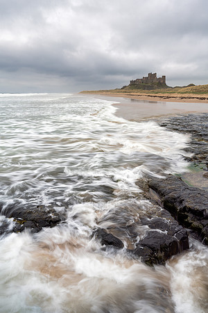 Waves crash against the rocks on the beach at Bamburgh Castle on a stormy day in Northumberland.