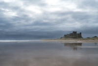 Bamburgh Castle reflected in the sand as the tide goes out at Bamburgh beach on a stormy day in Northumberland.
