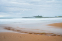 Ripples in the sand from the stream across Embleton bay beach across the waves with Dunstanburgh castle in the background. at Northumberland