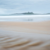 Ripples in the sand from the stream across Embleton bay beach across the waves with Dunstanburgh castle in the background. at Northumberland