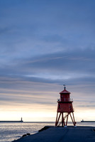 Sunrise at Tynemouth with Herd Groyne Lighthouse and Tynemouth lighthouse against an orange sky.