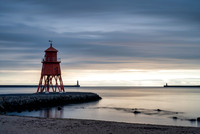 Sunrise at Tynemouth with Herd Groyne Lighthouse and Tynemouth lighthouse against an orange sky.