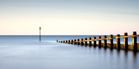 long exposure image of a sea bird sitting on the end of a groyne at sunrise on Dawlish Warren in Devon.