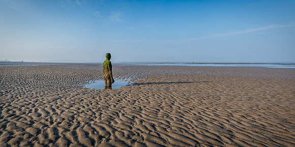 Statue of a man buried up to his knees on the beach at Anthony Gormley Another Place near Liverpool.