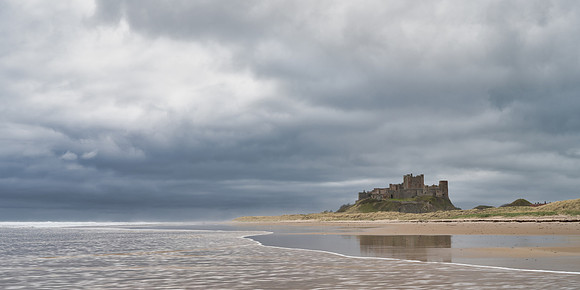 Bamburgh Castle reflected in the sand as the tide goes out at Bamburgh beach on a stormy day in Northumberland.