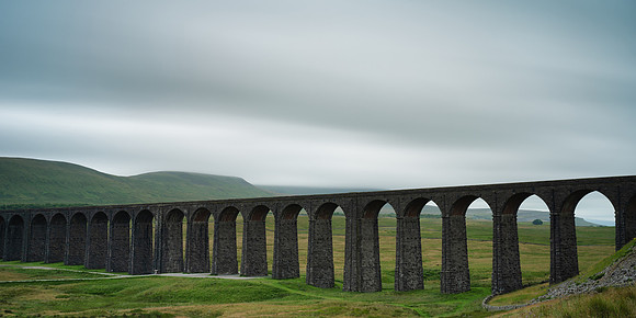Arches of the Ribblehead Viaduct stretch away across the valley on a dark stormy day.