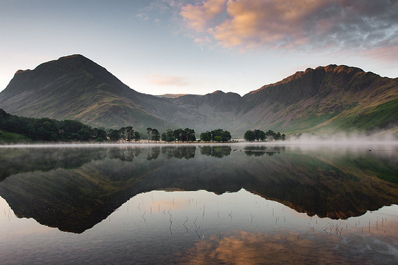 Misty sunrise image of Buttermere showing Haystacks Mountain in the background and ducks swimming across the lake.