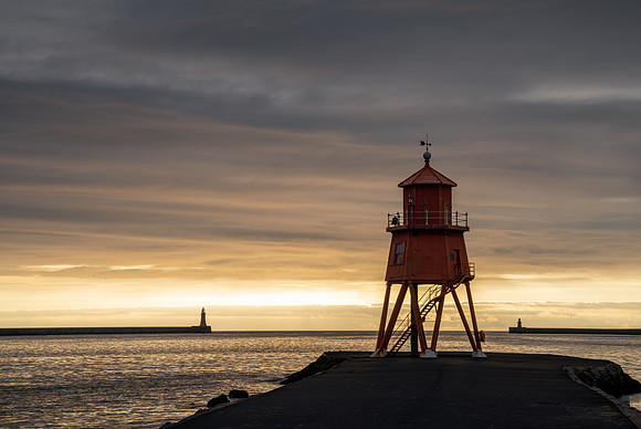 Sunrise at Tynemouth with Herd Groyne Lighthouse and Tynemouth lighthouse against an orange sky.