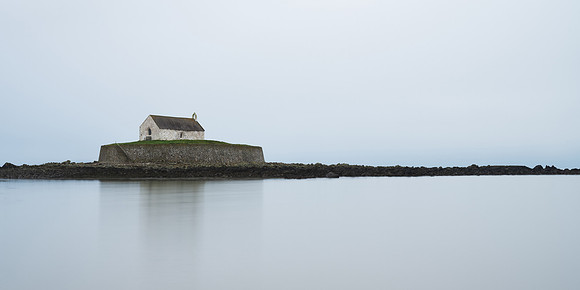 Porth Cwyfan Church reflected on the sea at high tide in Wales.