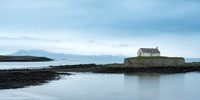 Welsh Mountains and Porth Cwyfan Church reflected on the sea at high tide in Wales.