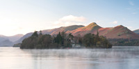 Derwent Isle is reflected in a calm misty Derwentwater infront of Catbells at sunrise during Autumn.